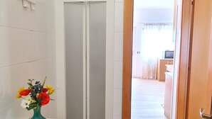 Ett badrum med en vit kakelbeklädd vägg, en blå vas med blommor, ett vitt skåp och en duschkabin.