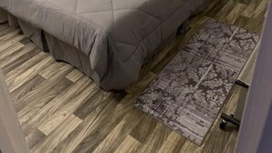 A bedroom with a grey bedspread, a patterned rug, and wooden flooring.