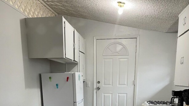 A compact kitchen with white cabinets, a refrigerator, a stove, and a dining table with chairs.