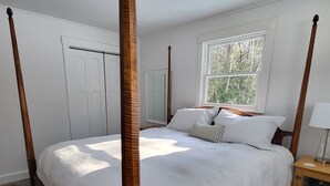 Ein Bett mit Baldachin, mit Holzrahmen, weißer Bettwäsche und Blick auf Bäume durch ein Fenster.