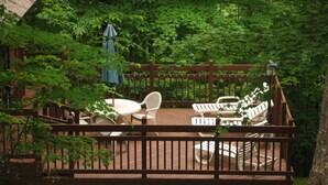 Um deck de madeira com móveis de exterior, incluindo uma mesa e cadeiras, rodeado por vegetação exuberante.