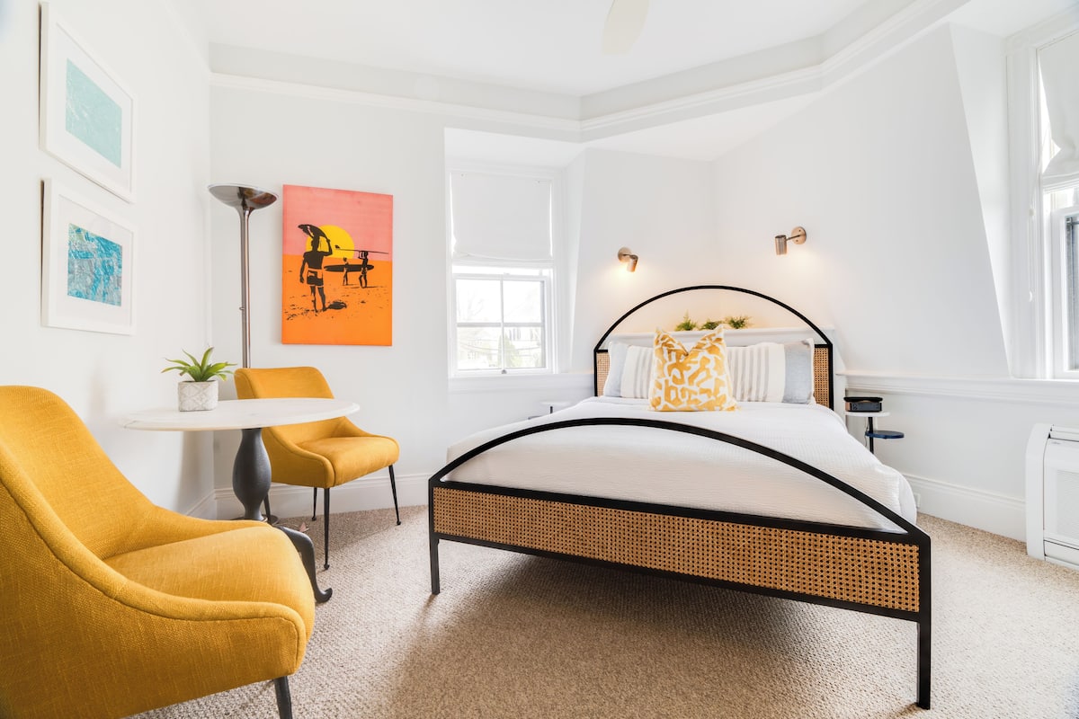 A bedroom with a bed, a chair, a table, and artwork on the wall.