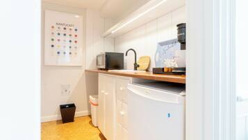 A modern kitchen with white cabinets, a microwave, a coffee machine, and a small trash bin.