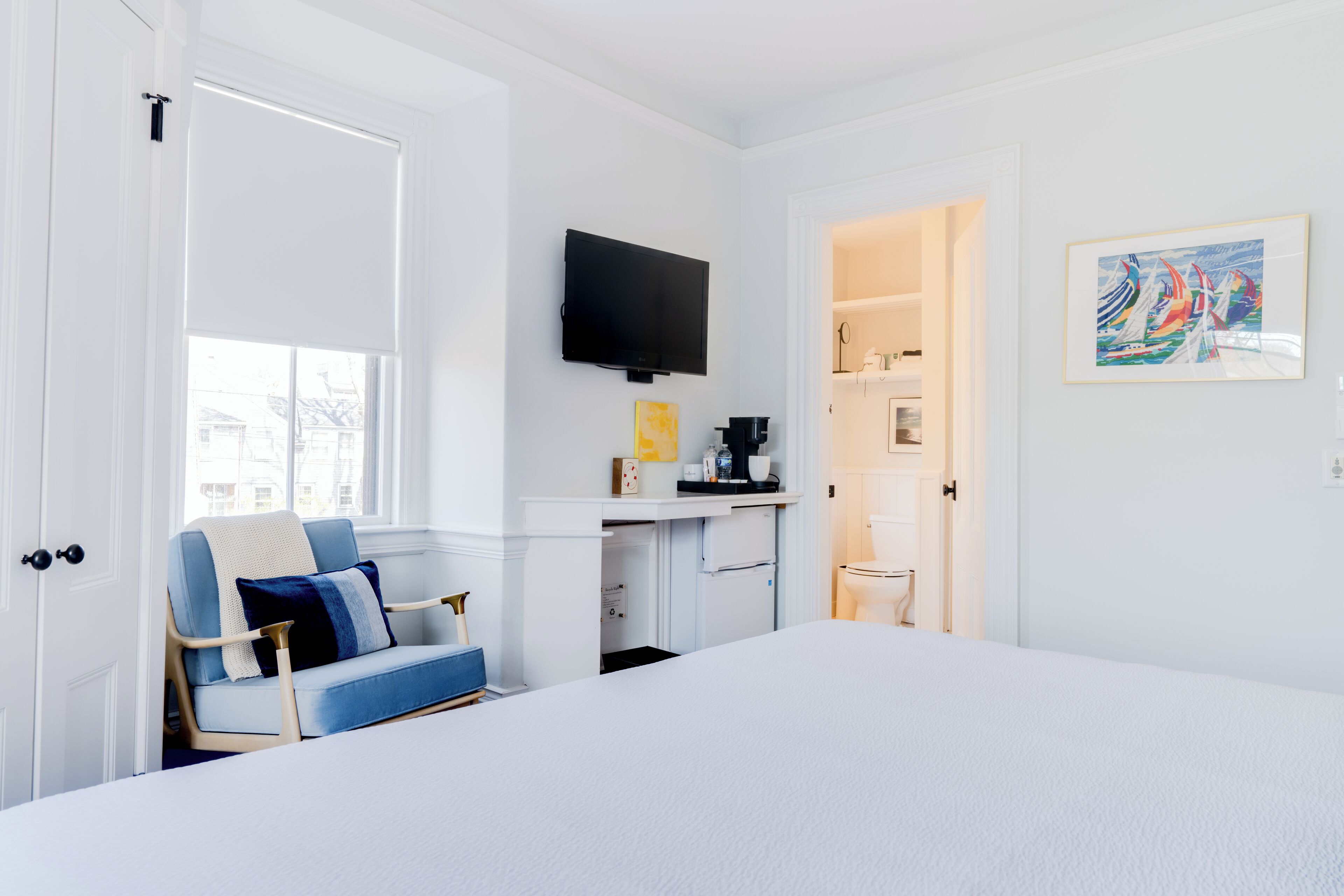 A hotel room with a bed, a desk with a flat-screen TV, a window, and a door leading to a bathroom.