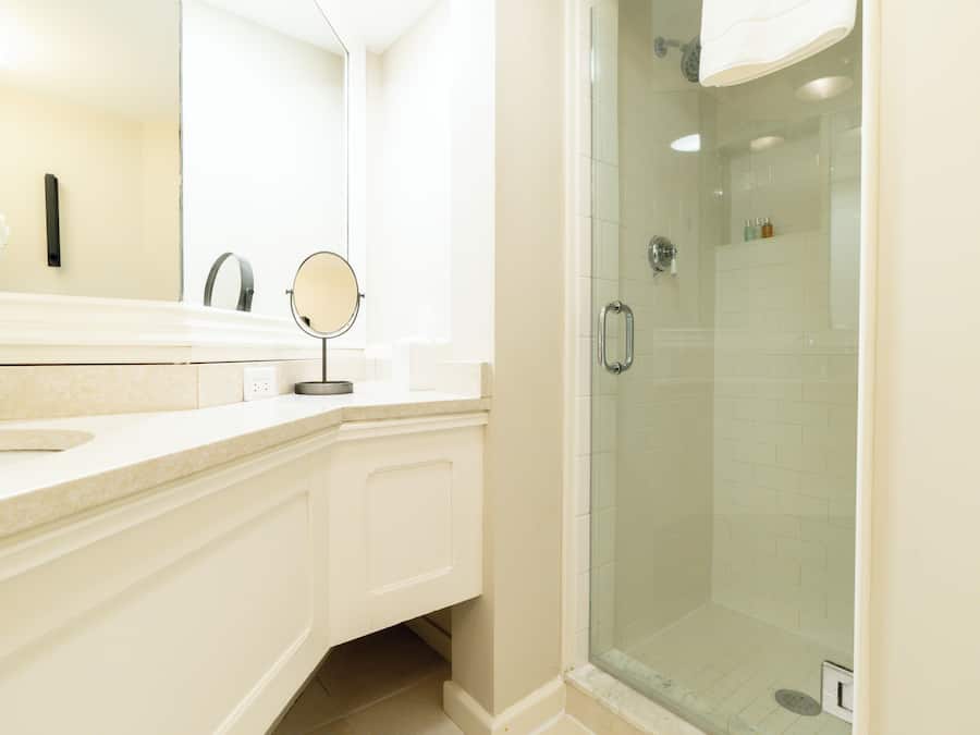 A modern bathroom with a glass-enclosed shower, a round mirror, and a white sink.