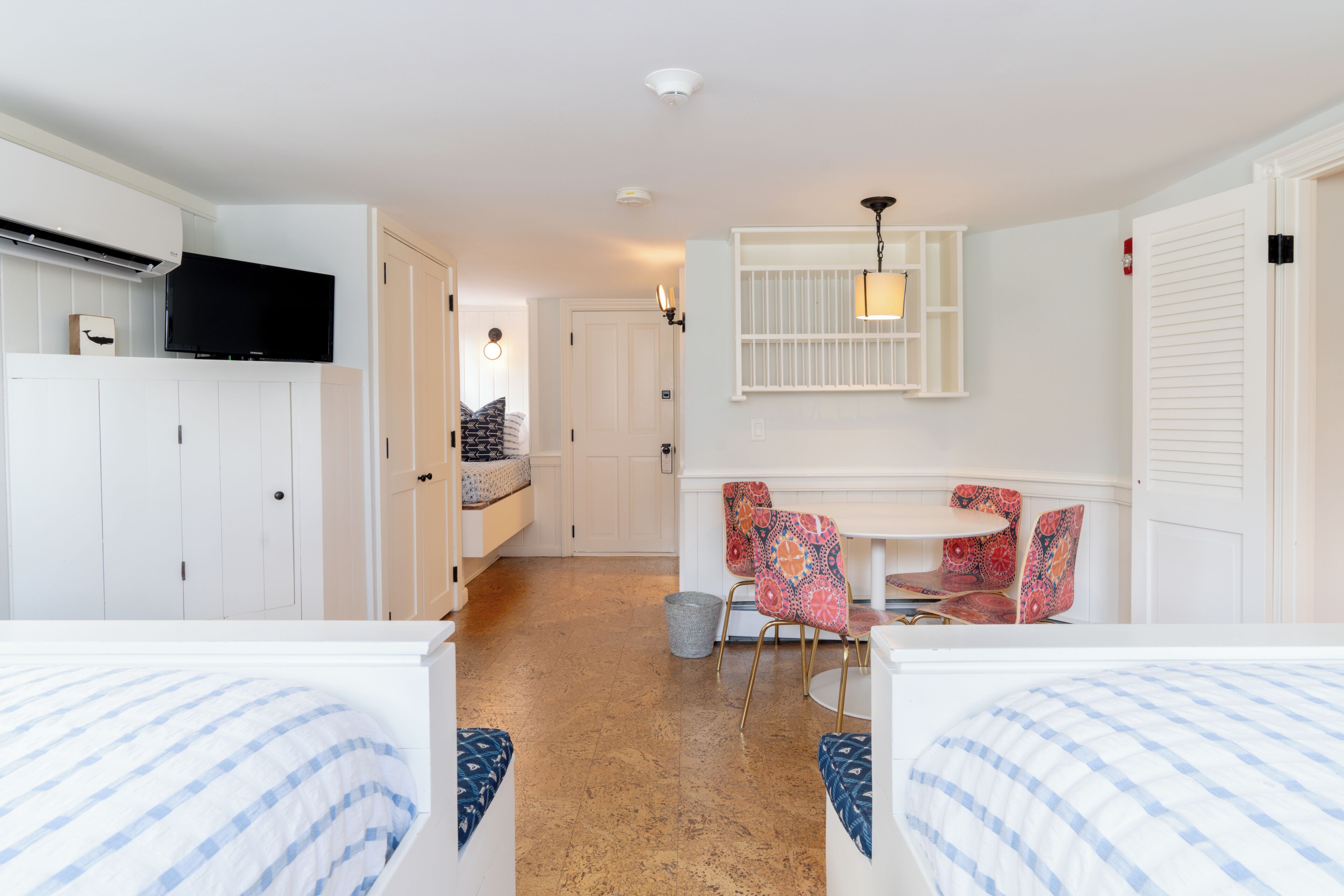 A hotel room with two beds, a TV, a dining area with a table and chairs, and a kitchen area.