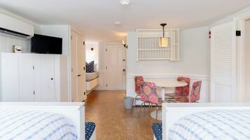 A hotel room with two beds, a TV, a dining area with a table and chairs, and a kitchen area.