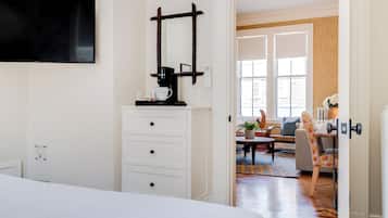 Une chambre d’hôtel avec un lit, un téléviseur fixé au mur, une machine à café et une vue sur l’espace de vie, accessible par une porte ouverte.