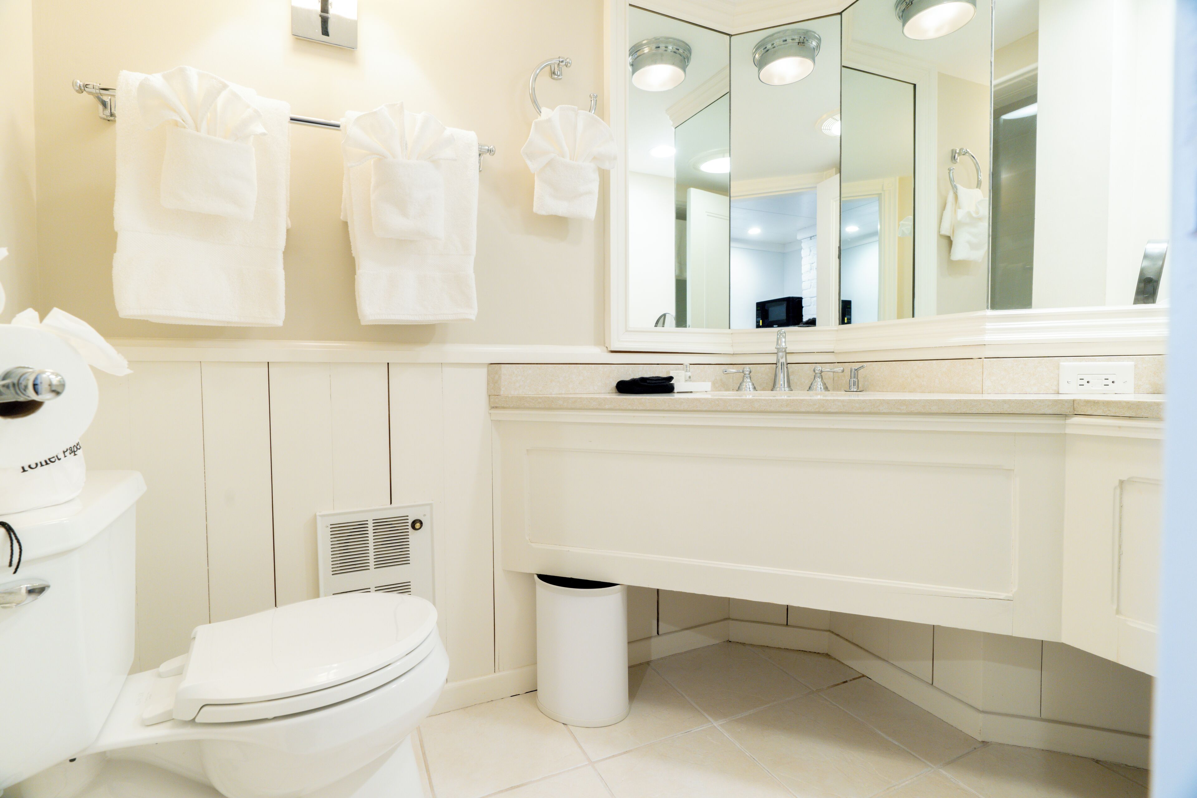 A modern bathroom with a toilet, sink, and mirror. There are towels hanging on a rack and a trash can under the sink.