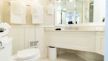 A modern bathroom with a toilet, sink, and mirror. There are towels hanging on a rack and a trash can under the sink.