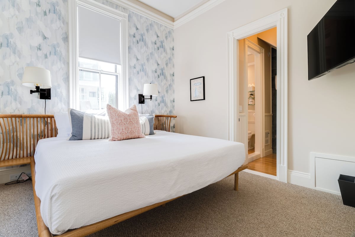 A bedroom with a large bed, two wall-mounted lamps, a TV, and a door leading to a bathroom.