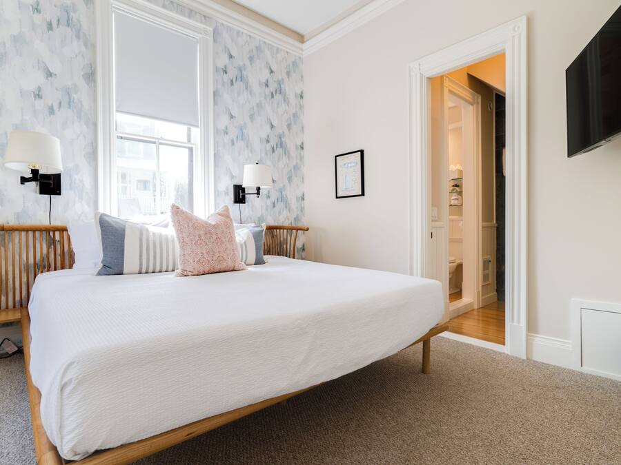 Un dormitorio con una cama grande, dos lámparas de pared, un televisor y una puerta que da a un baño.