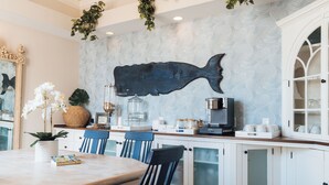 A dining area with a large fish-shaped wall art, white cabinets, and a wooden table. - Centerboard (Nantucket)