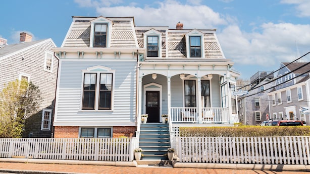A two-story building with a front porch, a staircase leading to the entrance, and a white picket fence. - Centerboard (Nantucket)