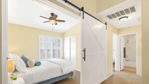 A bedroom with a bed, a ceiling fan, a sliding door, and a bathroom visible through an open door.
