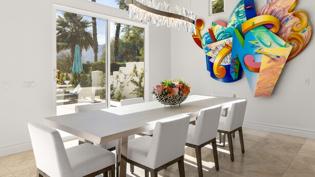 A modern dining area with a large window, white furniture, and a colorful abstract painting on the wall.