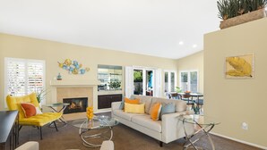 A living room with a fireplace, a sofa, a yellow armchair, and a glass coffee table.