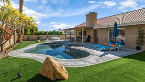 A backyard with a swimming pool, patio furniture, and a large rock.