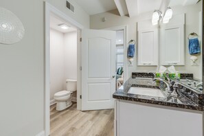 A modern bathroom with a white toilet, a sink with a granite countertop, and a mirror.