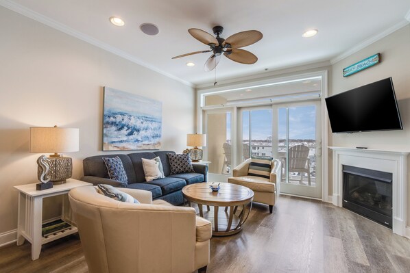 A spacious living room with a ceiling fan, a large TV, a fireplace, and a view of the city through large windows.