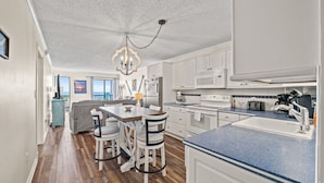 A modern kitchen with white cabinets, a blue countertop, and a chandelier. - Long Bay Dunes D2 - Oceanfront Condo w/Pool (Myrtle Beach)