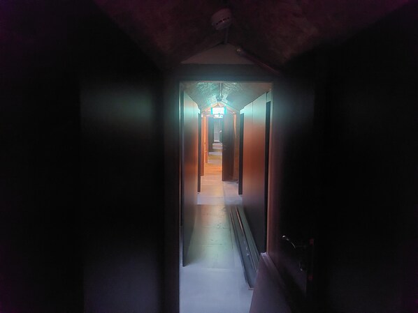 A narrow, dimly lit hallway with a staircase leading to a brightly lit area at the end.