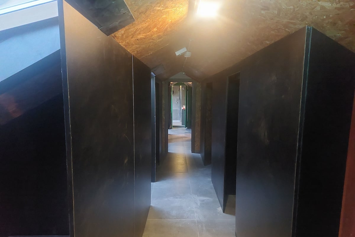 A narrow hallway with dark walls and a tiled floor, leading to a brighter area at the end.