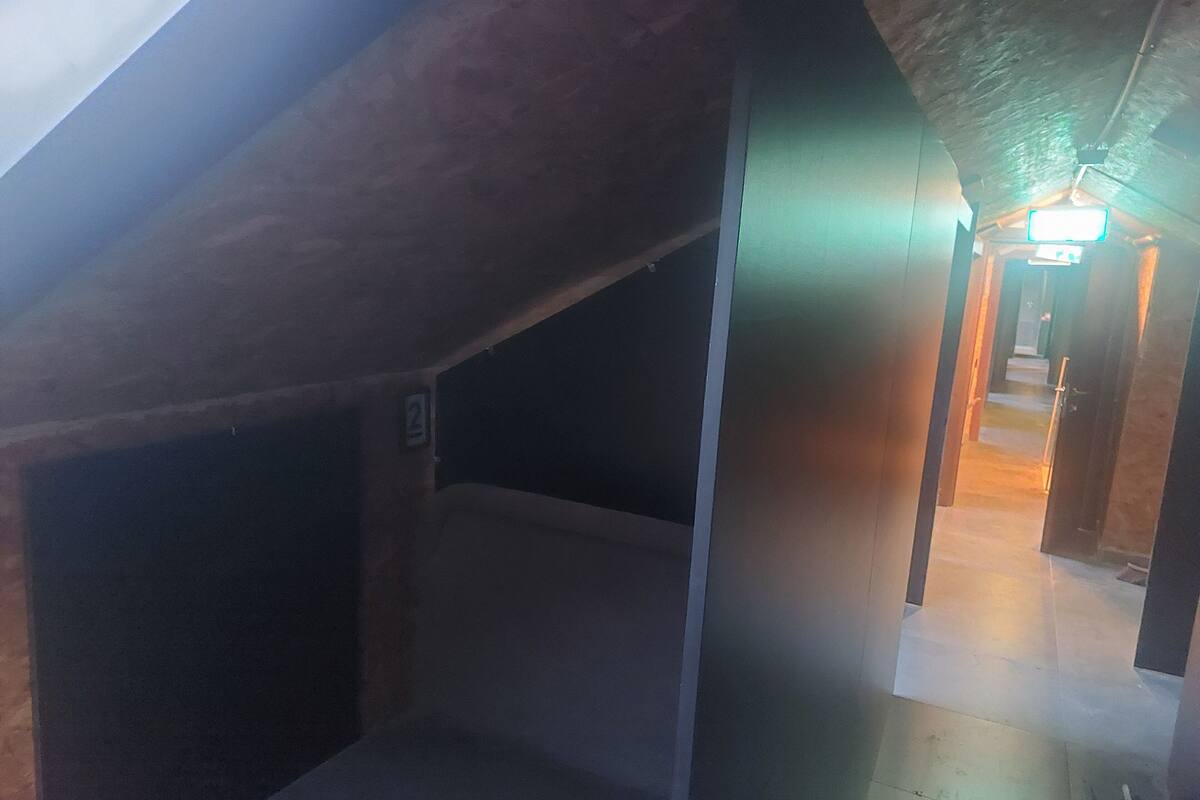 A dimly lit attic space with a sloped ceiling, a visible staircase leading to a lit area, and a number '2' sign on the wall.