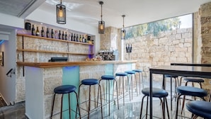 A bar area with a stone wall, wooden bar counter, and multiple stools. - malka hostel (Jerusalem)