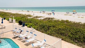 A beach view with a pool area, lounge chairs, and umbrellas.