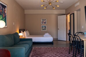 Een hotelkamer met een bed, een slaapbank, een eettafel met stoelen, een kroonluchter en kunstwerken aan de wanden.
