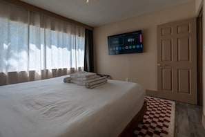 A hotel room with a bed, a flat-screen TV mounted on the wall, and a door. - Condo On The Beach - Heated Pool - Self Check-in (Belleair Beach)