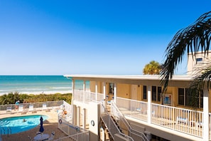 A beachfront hotel with a pool, a balcony with a railing, and a view of the ocean.