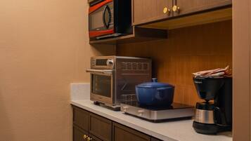 A compact kitchen with built-in appliances, including a microwave, toaster oven, and coffee maker, with wooden cabinets and a countertop.