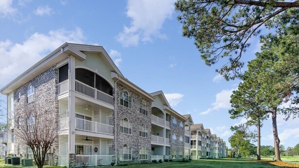 A multi-story hotel with balconies, stone facade, and a well-maintained lawn.