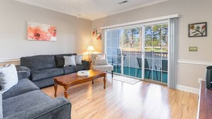 A living room with a grey sofa, a wooden coffee table, and a large sliding glass door leading to a balcony.