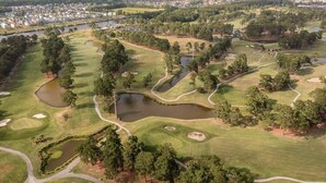 An aerial view of a golf course with multiple ponds, trees, and a town in the background.