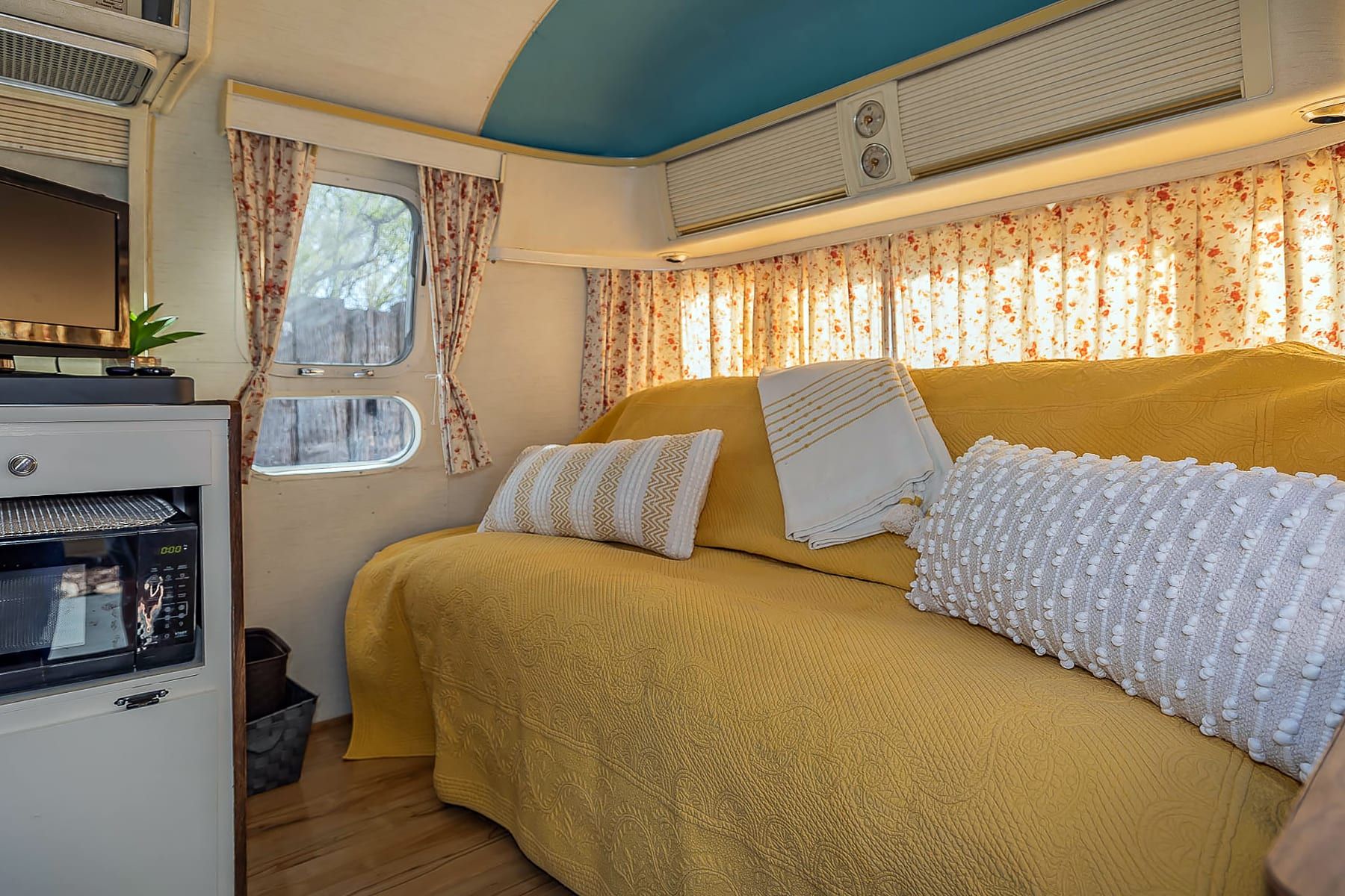 A cozy RV interior with a bed, a kitchenette, and a window with curtains.