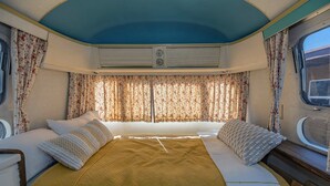 A cozy RV bedroom with a bed, curtains, and a window. - Economical and Private Tucson Tiny House (Tucson)