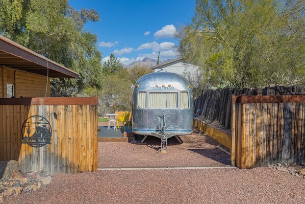 A vintage Airstream trailer parked in a rustic setting with a wooden fence and a sign reading "Casa Velo".