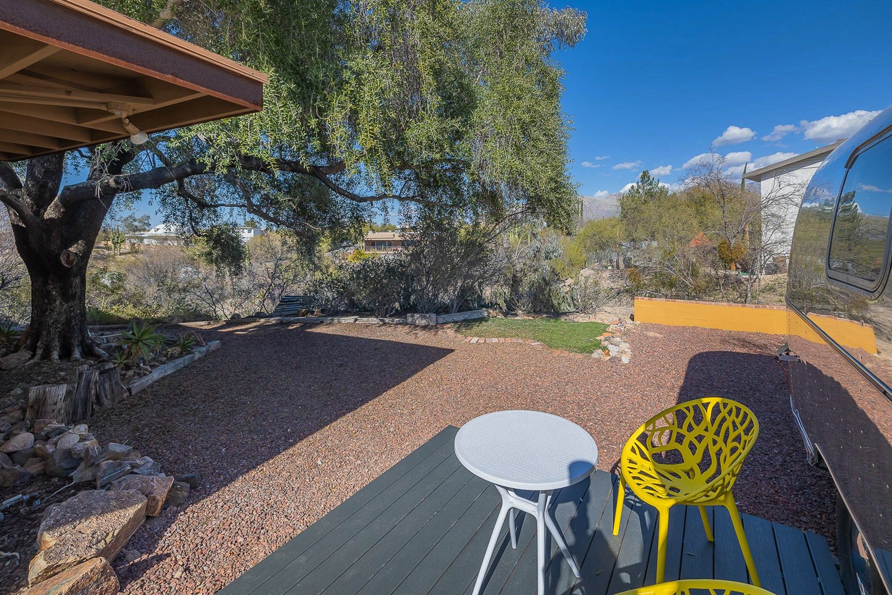An outdoor patio with a table and chairs, surrounded by a gravel area and trees.