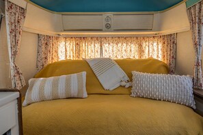 A bed with a yellow headboard, floral curtains, and two pillows.