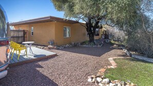 A single-story house with a brick exterior, a gravel driveway, and a tree in the yard. - Economical and Private Tucson Tiny House (Tucson)