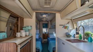 A compact RV interior with a kitchenette, two sleeping areas with blue bedding, and a small bathroom. - Economical and Private Tucson Tiny House (Tucson)
