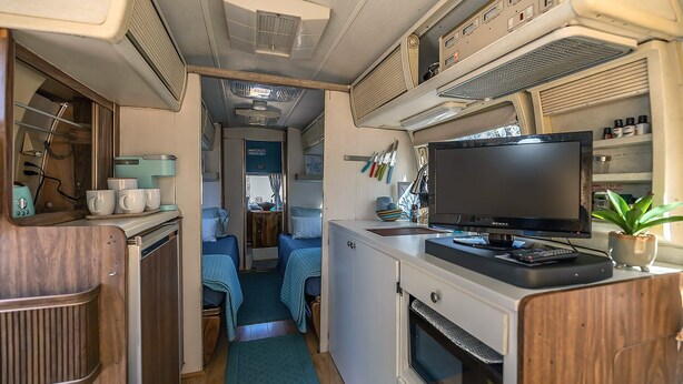 A compact RV interior with a kitchenette, a TV, and two sleeping areas. - Economical and Private Tucson Tiny House (Tucson)