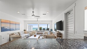 A spacious living area with a large granite island, comfortable seating, a flat-screen TV, and a view of the ocean. - Beach House - Family Tides by PHG (Panama City Beach)
