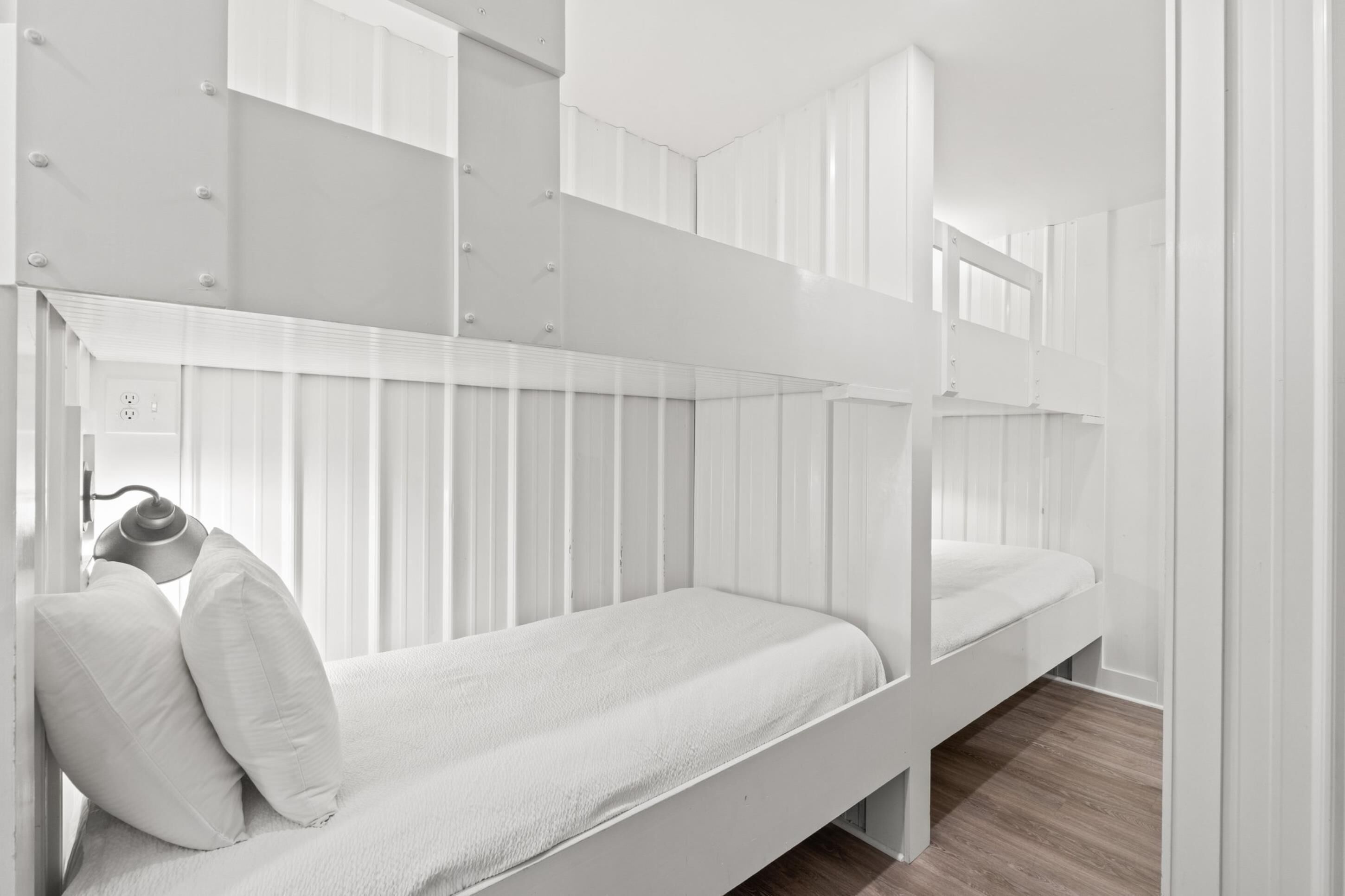 A bunk bed room with white bedding and a lamp.