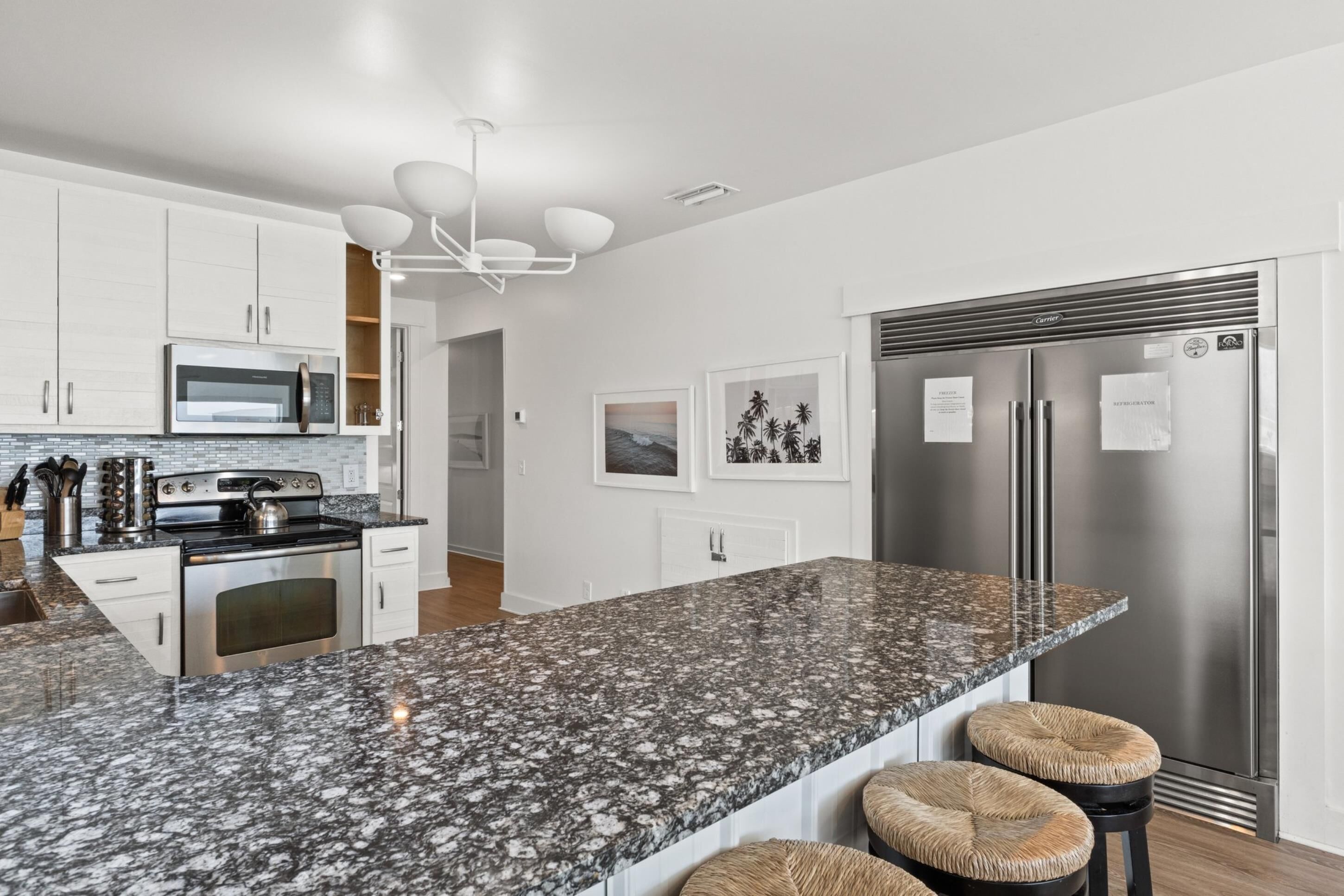 A modern kitchen with white cabinets, a granite countertop, stainless steel appliances, and a bar stool.