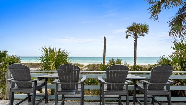 A patio with four Adirondack chairs facing a beach with a clear view of the ocean and palm trees. - Beach House - Family Tides by PHG (Panama City Beach)