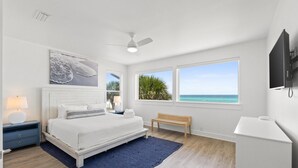 A bedroom with a bed, a bench, a TV, and a view of the ocean. - Beach House - Family Tides by PHG (Panama City Beach)